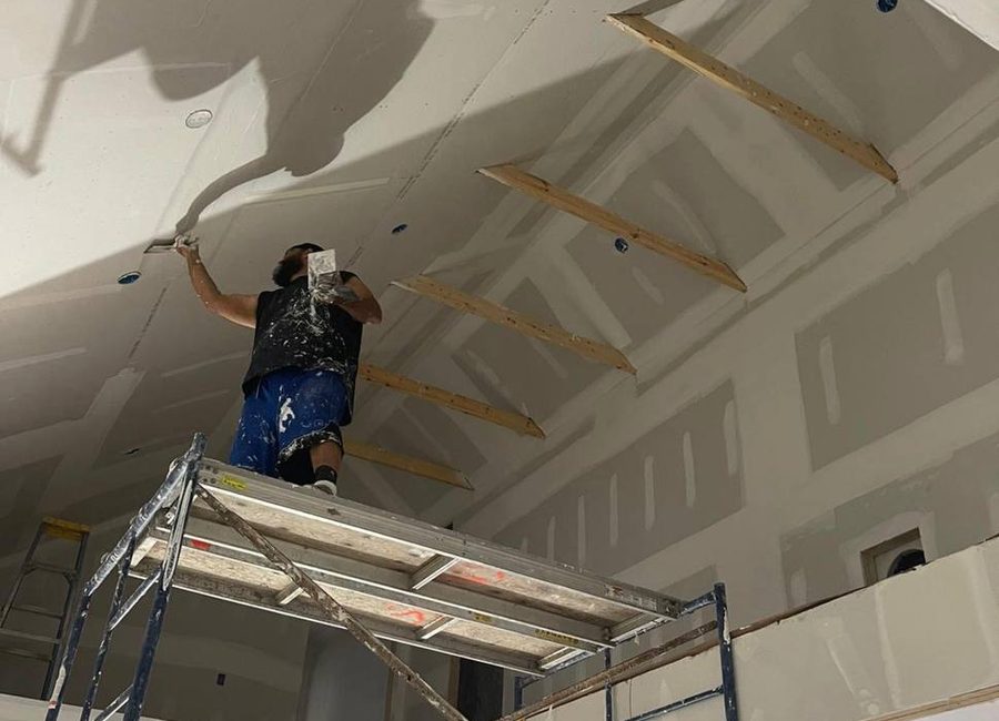 Mudline drywall finisher applying joint compound on a high ceiling from scaffold in a Louisville interior renovation